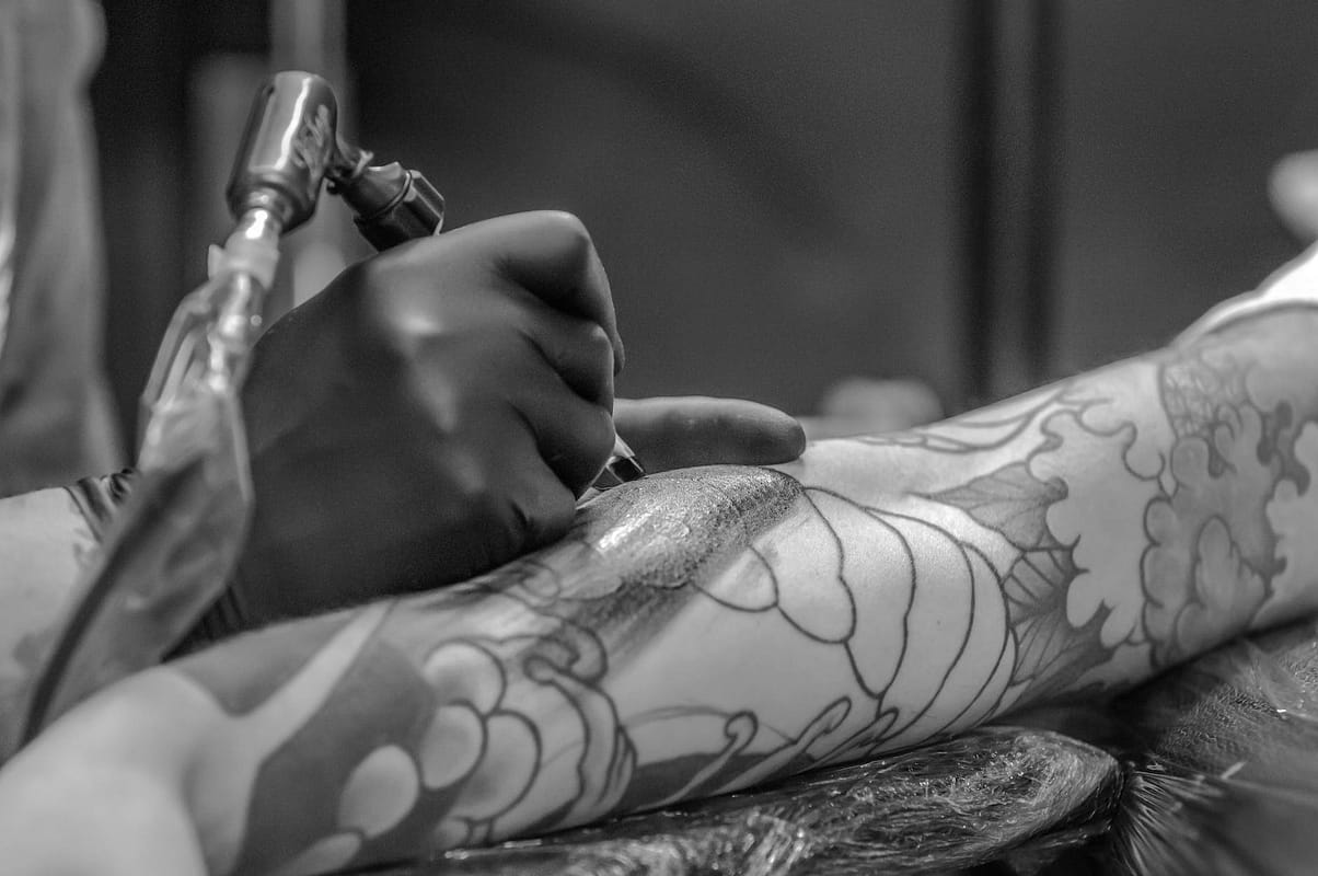 grayscale photo of person applying tattoo